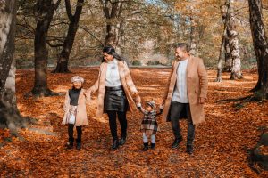 Family of 4 walking through an Autumn woodland with sun shining through the trees