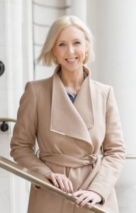 Image of a lady wearing a pink coat smiling at the camera .