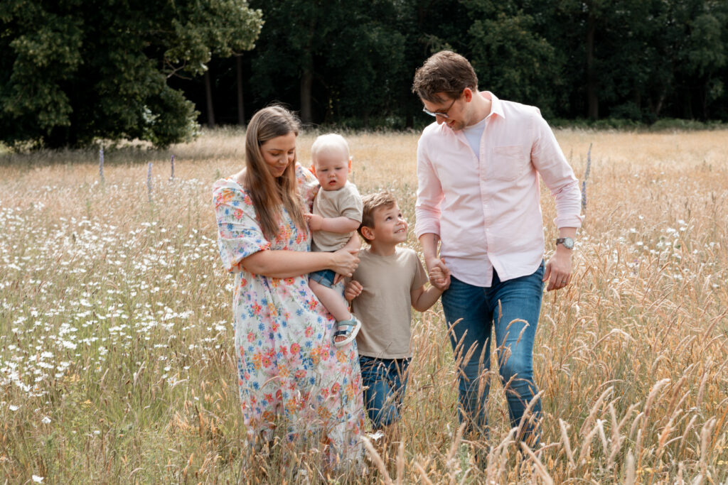 1I3A7981 Young family of four walking together in a summer meadow