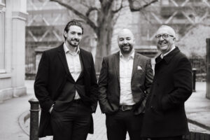 Black and white photo of a 3 men in a street smiling for their team photo