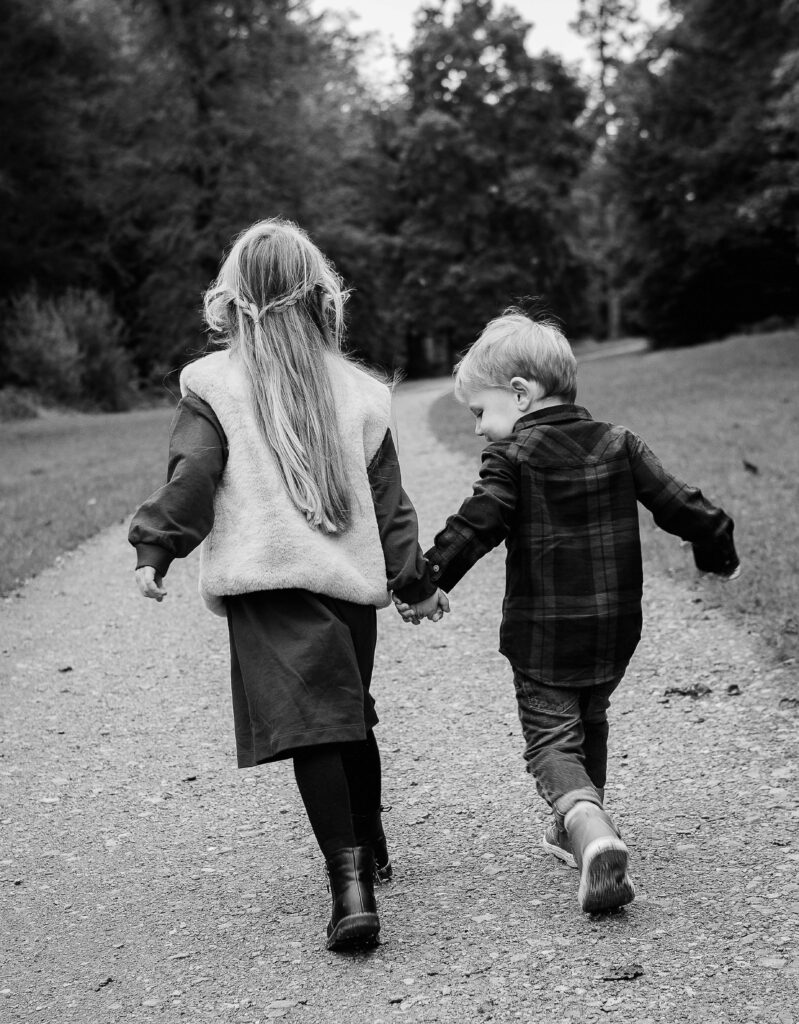 Black and white photo of a brother and sister running away holding hands.
