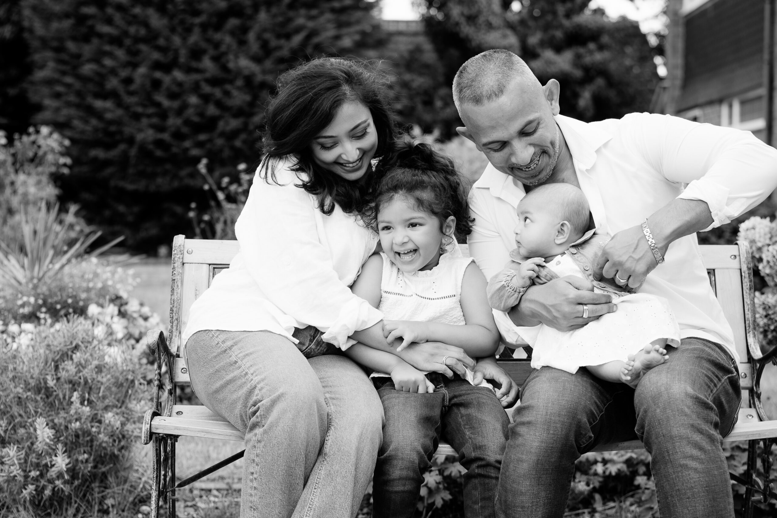 Black and white photo of a family laughing sitting on a bench outside their house