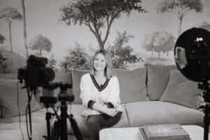 Behind the scenes photograph of Dr Gemma Roberts sitting on a sofa being filmed.