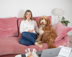 Woman sitting on sofa with her dog smiling at the camera
