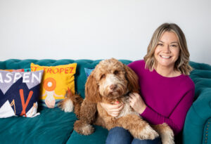 Woman sitting on sofa with her dog smiling at the camera