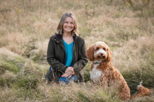 Lady sitting in a natural field smiling with her dog Elvis