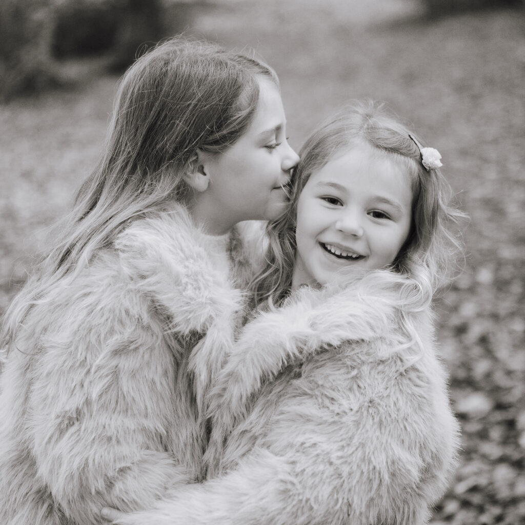 Black and White Image of two sisters. They are cuddling and one is looking at the camera laughing.