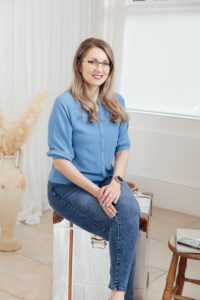 Lady sitting in a blue shirt and jeans looking at the camera smiling.