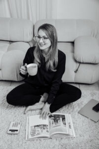 Woman sitting on the floor with a cup of coffee, laughing and looking at a book.